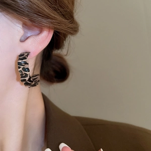 Close-up of leopard print C-shape earrings worn by a model in a brown blazer