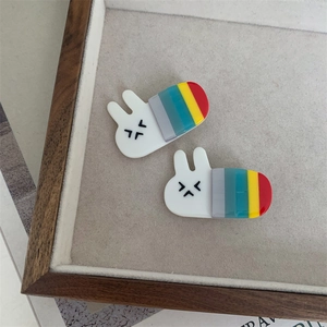 Pair of cute white bunny hair clips with colorful rainbow stripes on a wooden tray