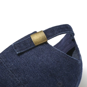 Close-up of dark blue denim baseball cap showing bronze metal buckle and fabric texture