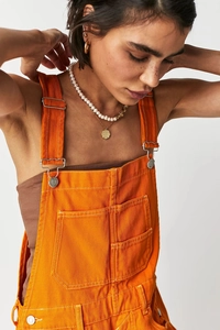 Detail shot of bright orange denim overalls showing white stitching and metal buckles