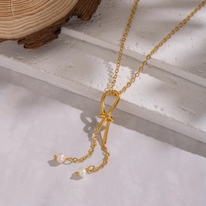 Detailed view of golden knot pendant necklace with two natural white pearls on wood surface