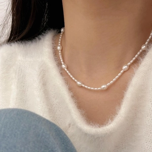 Detail of alternating white pearls necklace draped on model wearing a white sweater