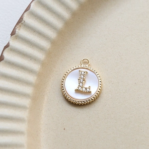 Close-up of gold-plated letter L pendant with cubic zirconia on a ceramic dish