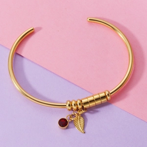 Detail of gold open bangle with red zircon birthstone and textured leaf pendant