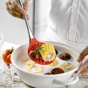 Red silicone slotted spoon with stainless steel handle lifting corn and mushrooms