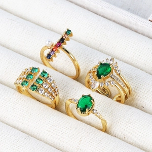 Detailed macro view of four gold-plated rings with emerald, zircon, and pearls on a tray
