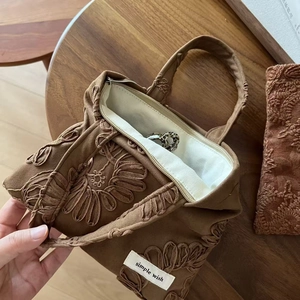Close-up of floral embroidery detail and brand label on a brown suede handbag