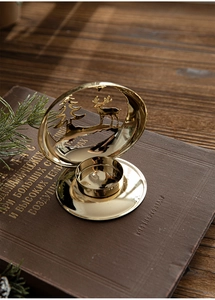 Close-up of golden iron candle holder with hollow reindeer and pine tree forest patterns