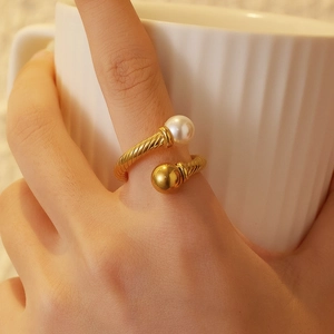 Detail of twisted 18k gold plated ring with white pearl and gold bead on hand