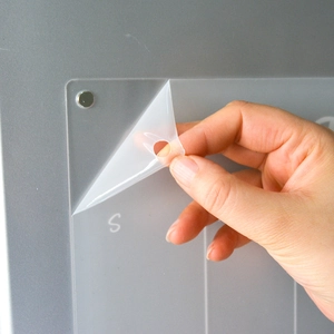 Close-up of removing protective film from magnetic acrylic weekly planner on a fridge