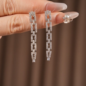 Gros plan de boucles d'oreilles chaîne en argent serties de cristaux tenues à la main