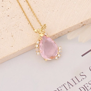 Detailed macro of a pink teardrop gemstone necklace with a gold fairy pendant wing design
