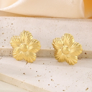 Dettaglio di orecchini a girasole dorati con petali testurizzati su pietra beige
