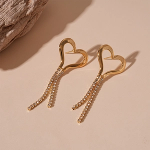 Macro shot of gold heart tassel earrings with white rhinestones on warm beige surface