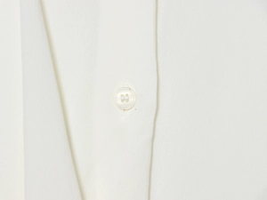 Macro shot of a pearlized button detail on a white long-sleeved asymmetrical blouse