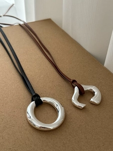 Close-up of polished silver circular and C-shape pendants on leather cord necklaces