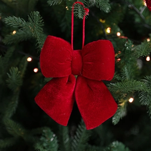 Elegant red velvet Christmas bow hanging on a green tree with warm festive bokeh lights
