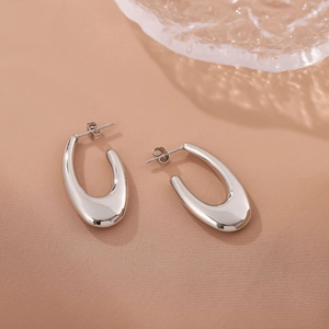Minimalist silver hollow oval earrings in stainless steel on a warm textured backdrop
