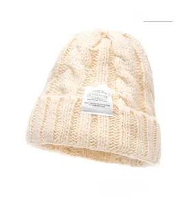Detail of beige chunky knit beanie showing cable pattern and white rectangular fabric label