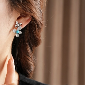 Detailed view of silver flower earrings with teal gems and zircons worn by a model