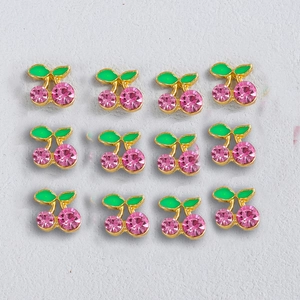 Macro shot of 12 cherry nail charms with pink crystals and green enamel leaves