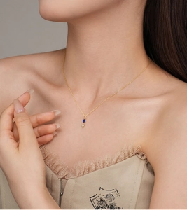 Close-up of gold chain with blue teardrop and white zircon pendant on female neck