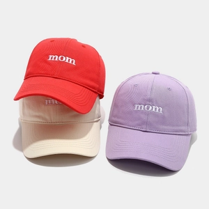 Detail of embroidered 'mom' text on cotton baseball caps in red, beige and purple
