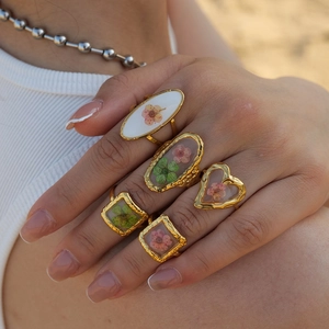 Detail of five gold rings with dried pink flowers in resin, worn on a model hand