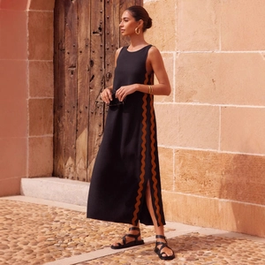Black sleeveless maxi dress with contrast wavy trim and side slit in Mediterranean setting