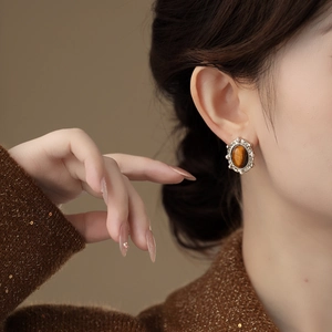 Close-up of a model wearing oval tiger eye earrings with vintage filigree details