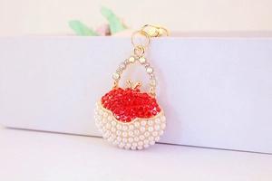 Close-up of a handbag-shaped keychain featuring red rhinestones and white pearls on metal