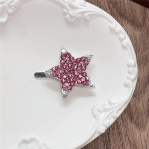 Macro view of a silver star hair clip with pink and clear rhinestones on a ceramic plate