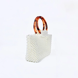 Detail of handmade pearl beaded handbag with amber acrylic ring handles and square profile