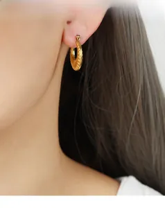 Detail of vintage gold-plated geometric textured hoop earrings worn by a model