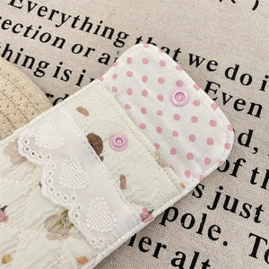 Close-up of quilted cotton pouch with lace detail, floral pattern, and pink snap button
