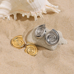 Dettaglio orecchini a spirale in oro 18K e argento su sabbia con decoro marino