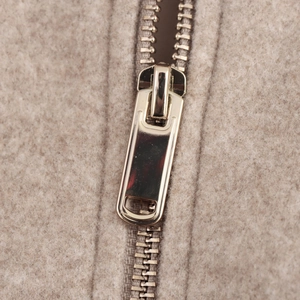 Detail shot of a golden metal zipper on a beige wool bomber jacket for women