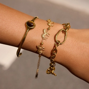 Close-up of stacked gold titanium bracelets featuring tiger eye stone and zebra charms