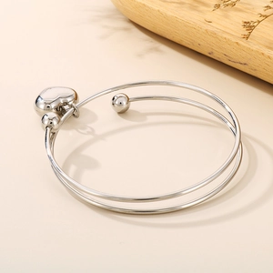Detail view of silver heart pendant double-layer open bangle on wooden tray decor