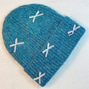 Close-up of peacock blue knitted beanie featuring white and lavender ribbon bow details
