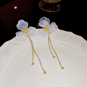 Elegant white acrylic flower earrings with long gold tassels on a white ceramic plate