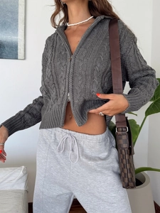 Detail of grey cable-knit cardigan with zipper closure on a female model outdoors