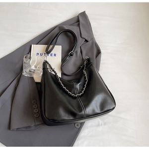 Detail of black hobo bag with silver chain and white stitching on a grey blazer