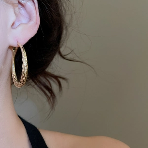 Close-up of gold twisted hoop earrings with woven texture on a female model