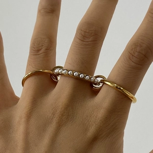 Detailed view of interconnected 18K gold rings with white pearls on a model hand