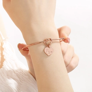Detail eines Roségold Love Herz Charm Armbandes mit Knotendesign am Handgelenk