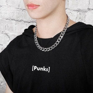 Detail of a thick silver Cuban link necklace worn by a model on a white brick background