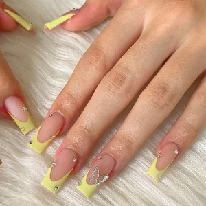Yellow French tip press-on nails with butterfly rhinestone charms on white plush