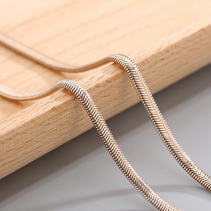 Macro shot of rose gold flat snake bone chain with polished metallic texture on wood