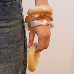 Detail von vier Kunstharz-Armreifen in Bernstein, Creme und Klar an einem Model